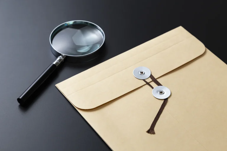 Manila envelope and magnifying glass on a dark desk, illustrating document review in divorce discovery